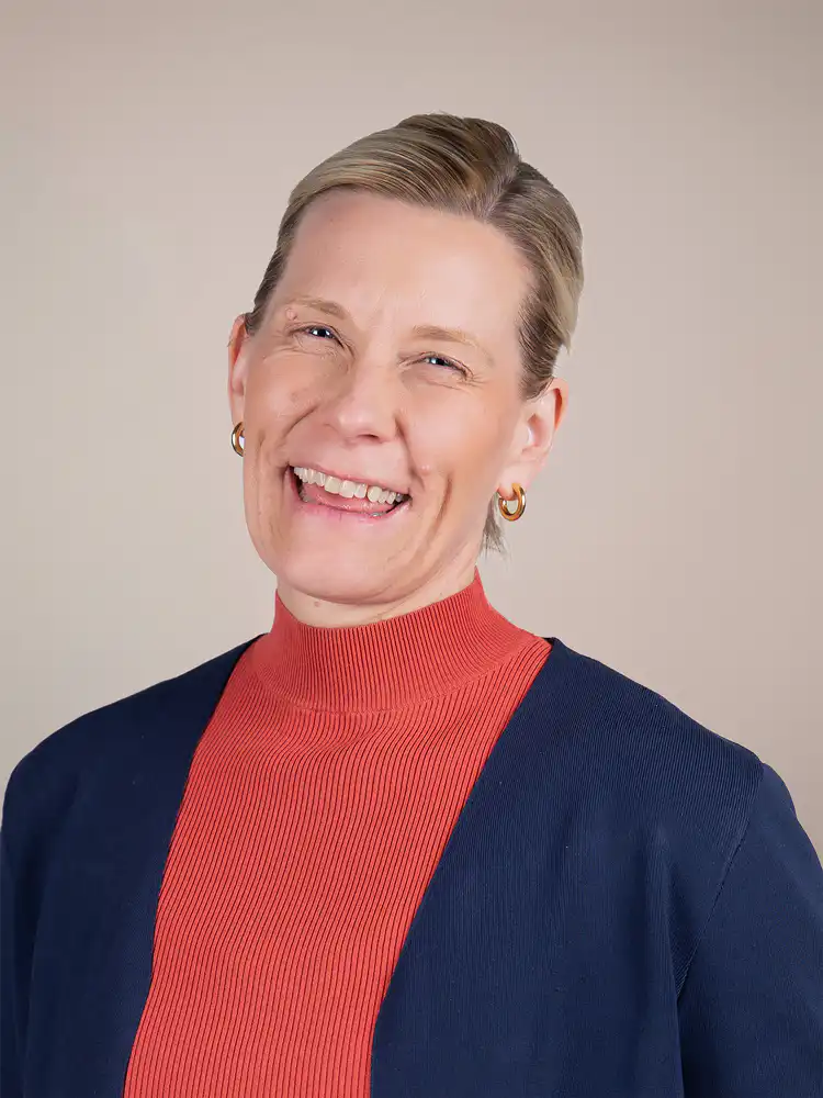 Smiling woman with short blonde hair wearing a red turtleneck and a navy cardigan, facing the camera.