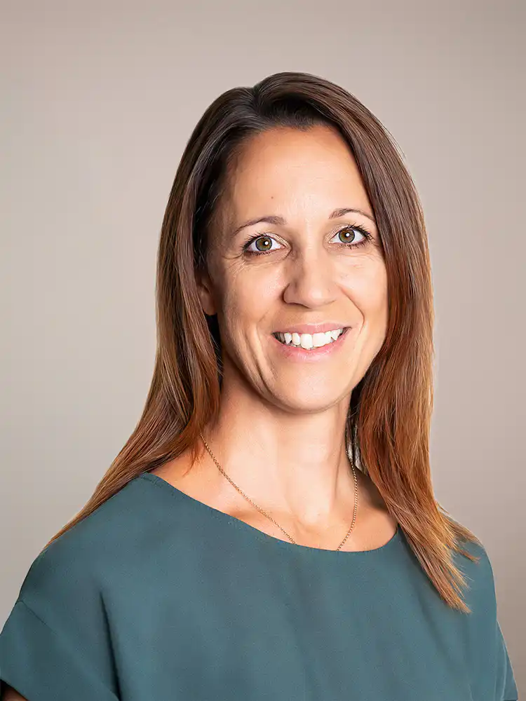 Head-and-shoulders portrait of a smiling woman with shoulder-length brown hair wearing a teal blouse against a neutral background.