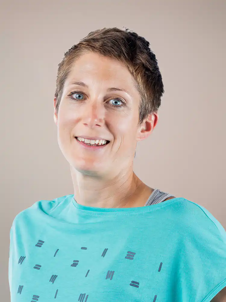 Smiling woman with short hair wearing a turquoise T-shirt, facing the camera