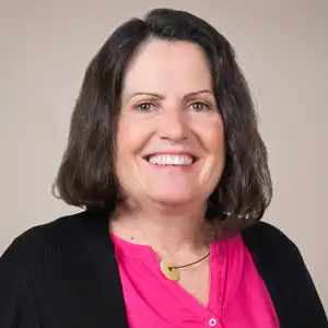 Smiling woman with shoulder-length dark hair, wearing a pink blouse and black cardigan.