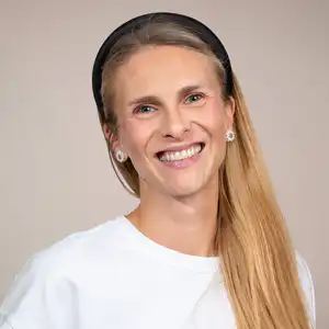 Portrait of a smiling woman with long blonde hair, wearing a white top and a black headband, facing the camera.