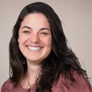 Portrait of a smiling woman with long dark hair against a beige background.