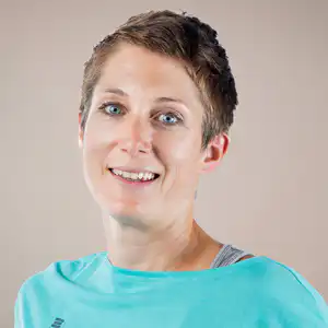 Portrait of a smiling woman with short light brown hair wearing a turquoise shirt against a neutral background, looking at the camera.